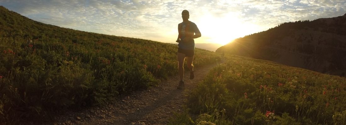 Coureur en trail sur un sentier de montagne au lever du soleil, entraînement running 2025 pour endurance et perte de poids.