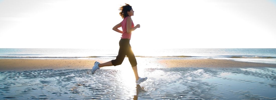 Femme courant sur la plage au lever du soleil, symbole d’hydratation et de performance en course à pied.