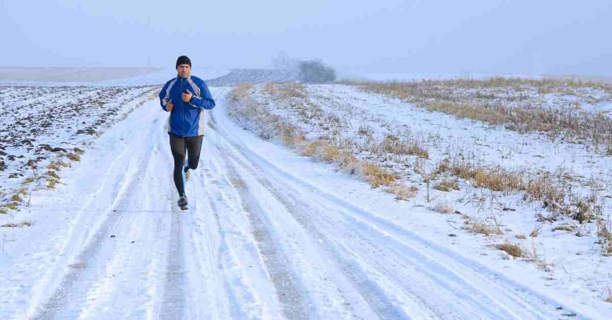 coureur en tenue running hiver sur route enneigée avec veste thermique et équipement contre le froid